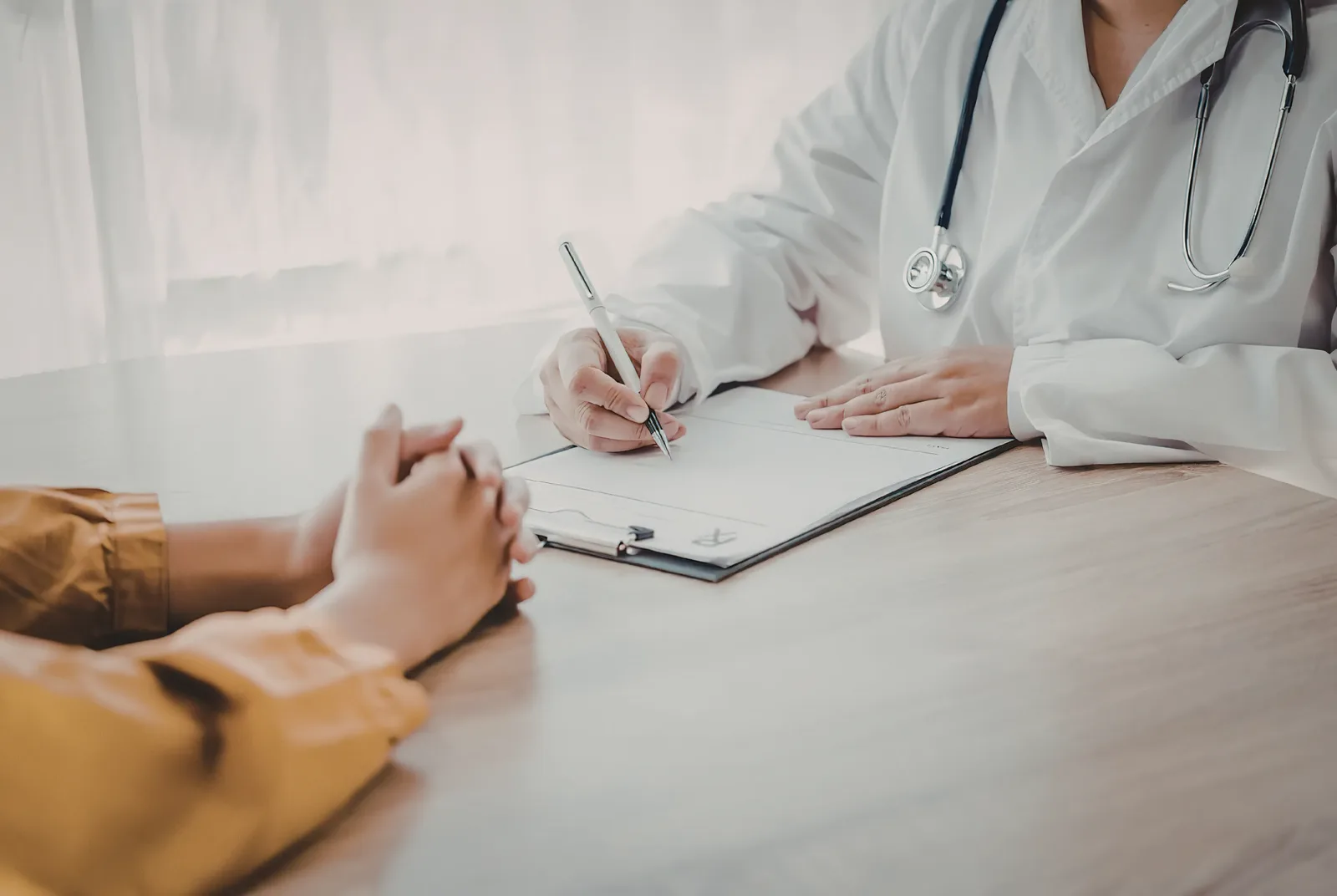 A practitioner and a client seated across a desk in conversation, with notes being written.