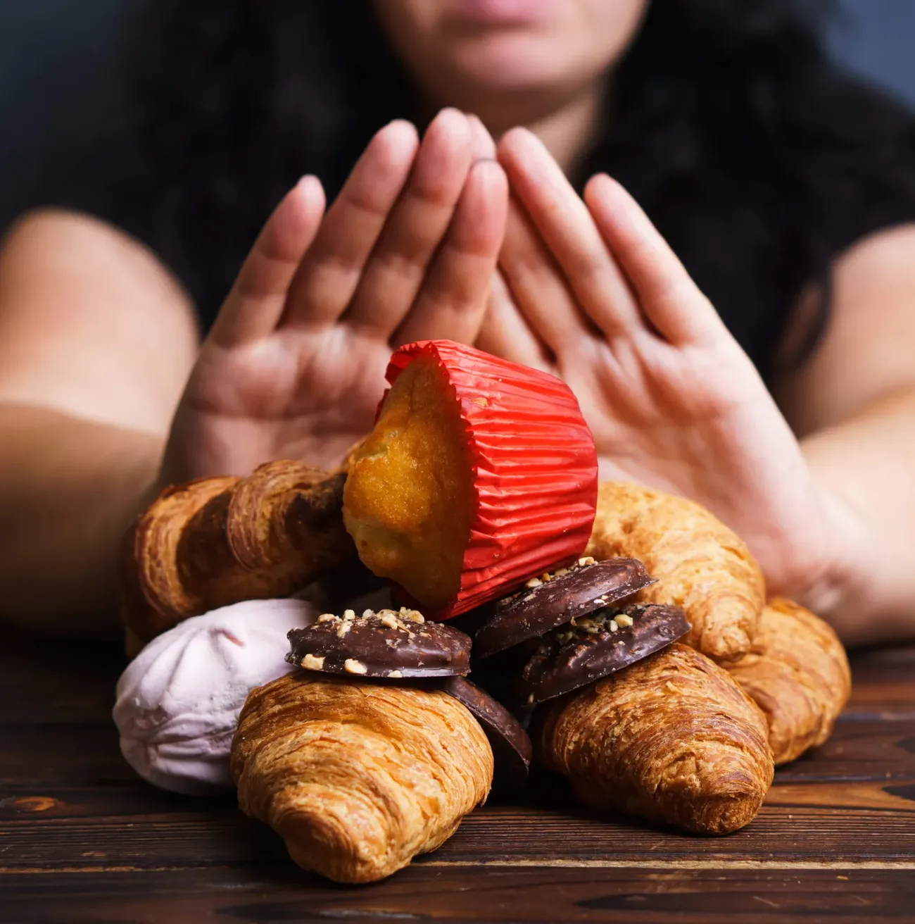 A person pushing away a plate of pastries and chocolates with both hands, in a gesture of refusal.